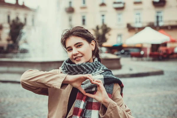 Молода дівчина на вулиці показує серце з пальцями, тому що вона любить місто і подорожує так багато . — стокове фото