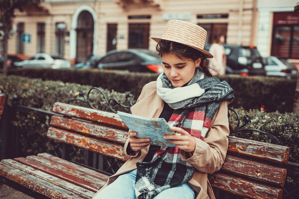 Lovely tourist got lost in a foreign city and looks at a map to find way out while sitting on a bench.