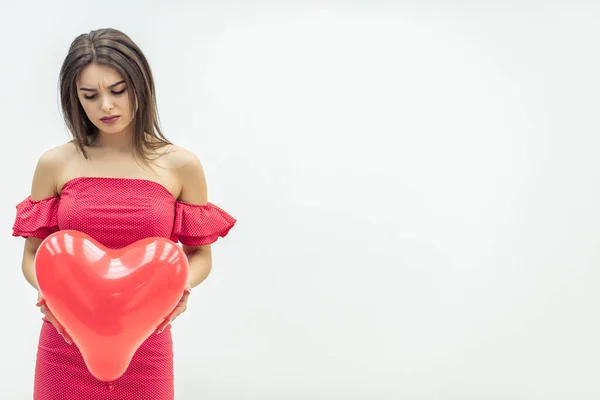 Menina perturbada está segurando balão coração vermelho enquanto pensa sobre o amor não correspondido ou rompimento . — Fotografia de Stock