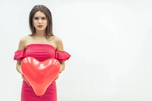 Menina perturbada está segurando balão coração vermelho enquanto pensa sobre o amor não correspondido ou rompimento . — Fotografia de Stock