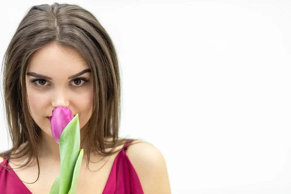 Gros plan de la jeune femme mignonne sentant la tulipe rose, souriant légèrement à la caméra, regardant paisiblement. — Photo