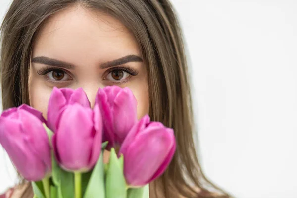 Cropped shot of beautiful girl in the maroon dress smells tender tulips over white background.