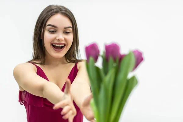 Joyeuse femme étendant les mains pour obtenir un tas de tulipes et souriant sur un fond blanc. — Photo