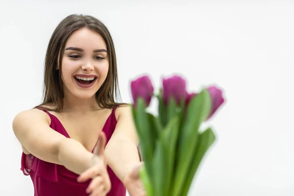 Joyeuse femme étendant les mains pour obtenir un tas de tulipes et souriant sur un fond blanc. — Photo