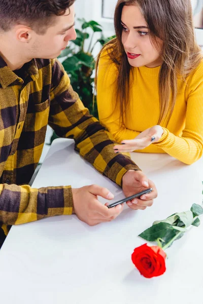 Taille-up portret van jonge man met behulp van telefoon en vrouw trekken zijn hand, vragen hem om haar aandacht te geven. — Stockfoto