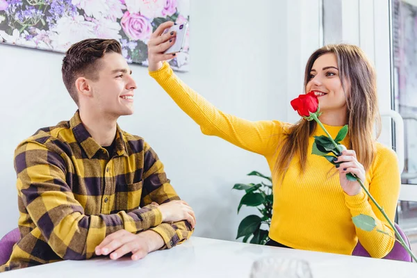 Boldog fiatal lány szelfit készít vörös rózsával, amit a barátja adott neki. A fiú nagyon boldog, hogy ilyen reakciót lát a jelenére.. — Stock Fotó