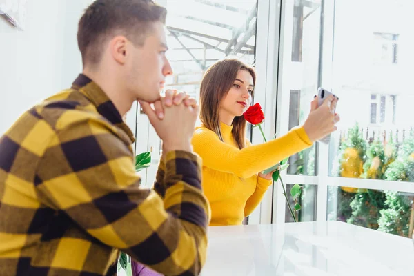 Muchacho molesto esperando, mirando desaprobadamente, mientras su amigo sucio se hace selfie con rosa roja él la trajo . — Foto de Stock