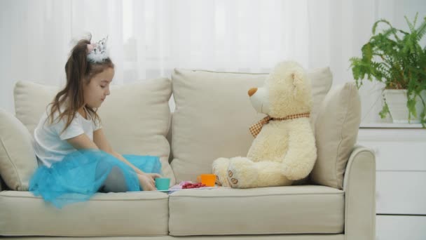 왕관과 드레스를 입은 귀여운 소녀, 그녀의 가장 친한 친구 테디 베어에게 차마시는 법을 가르쳐 준다. 하지만 장난감은 살아 있지 않습니다.. — 비디오