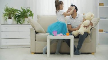 Tatlı prenses kız babasını güzelleştiriyor, kafasına taç takıyor. Babam ayıyı dizlerinin üstünde tutuyor..