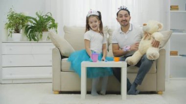 Baba, kız ve Teddy çay partisi veriyorlar. Onlar kanepede oturuyorlar. Babam el sallıyor Teddy 'nin patisinden merhaba diyor.