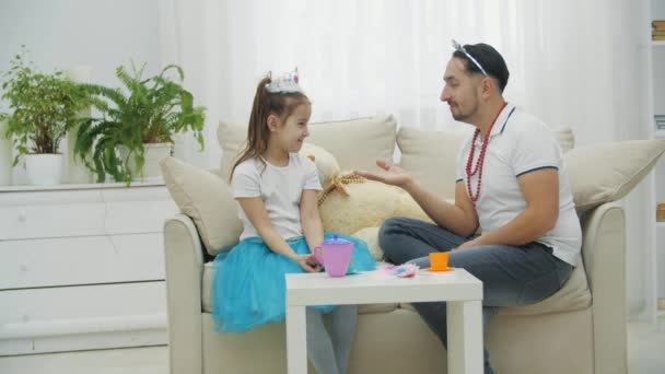 Father and daughter playing in princesses. Funny man kissing girls hand, then pretending to bite it. He hugs her and breaks a crown. Tears on babys eyes. — Stock Video
