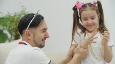 Küçük bir çocuk fırça tutuyor, babası için makyaj yapıyor, o da ellerini itiyor..