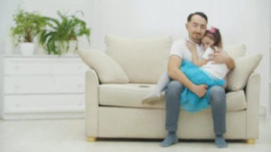 Komik babanın kanepeye oturup, küçük uykulu kızını dizlerinin üzerine çöktürdüğü bulanık bir video..