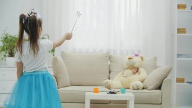 Küçük peri elinde sihirli değnekle kanepede oyuncak ayısını büyülüyor, sonra kameraya dönüyor, önünde asasını sallıyor, gülümsüyor..