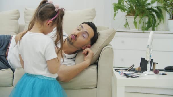 Słodkie małe dziecko robi makijaż dla jej tatuś, nakładając różową szminkę na jego usta podczas gdy on śpi. — Wideo stockowe