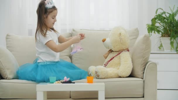 Cute girl w koronie i sukience, noszenie opaski na Teddy Bear, picie herbaty. — Wideo stockowe