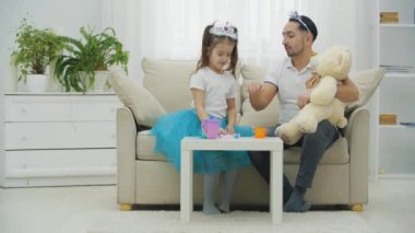 Tatlı prenses kız babasını güzelleştiriyor, kafasına taç takıyor ve eline de el bandı takıyor. Babam ayıyı dizlerinin üstünde tutuyor..
