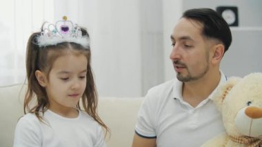 Şirin prenses kızın babasını güzelleştirdiği ve kafasına taç taktığı yakın plan. Babam oyuncak ayının arkasına saklanıyor..