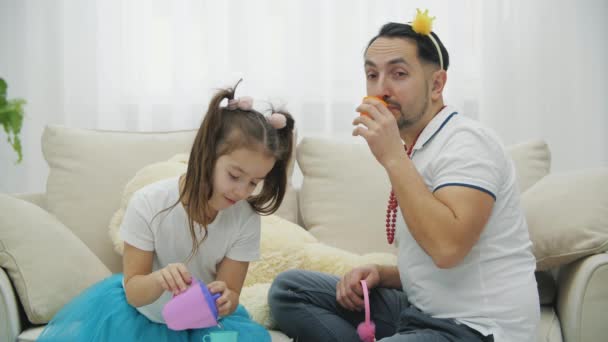 面白いパパと娘の演奏、おもちゃのカップからお茶を飲む、美しいヘッドギアを身に着けて. — ストック動画