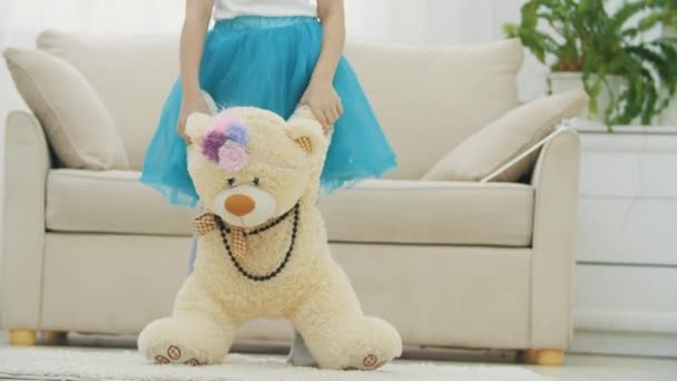 Ragazzina ritagliata in piedi gonna blu, tenendo un peluche orsacchiotto in collana e copricapo divertente. — Video Stock