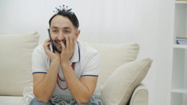Yakışıklı bir genç adam telefonda konuşuyordu. Komik bir taç, kolye ve etek giyiyor..