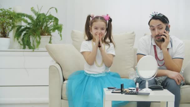 Snygg ung man pratar i telefon. Hans dotter viftar med en borste nära ansiktet och nyser på grund av ansiktspulver.. — Stockvideo