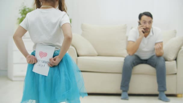 4k wideo małej dziewczynki ukrywającej prezent i pocztówkę za plecami dla ojca. — Wideo stockowe