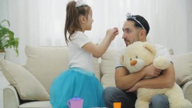 Kızı, babasının kafasındaki tacı yeniden ayarlıyor. Şirin prenses kız, prenses babası ve ayıcığı çay partisi veriyor..