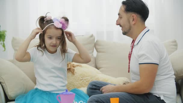 Papi e hija divertidos jugando en princesas, sentados en el sofá, usando sombreros. — Vídeo de stock