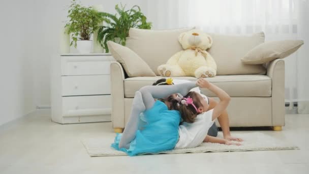Маленька мила дівчинка робить вправи на килимі. Її батько грає біля неї. Вони носять смішні головні убори . — стокове відео