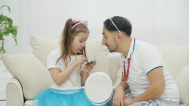 Babası komik bir şekilde ellerini sallıyor. Bu arada küçük çocuk onun için makyaj yapıyor. Göz kapaklarına menekşe rengi gölgeler sürüyor..