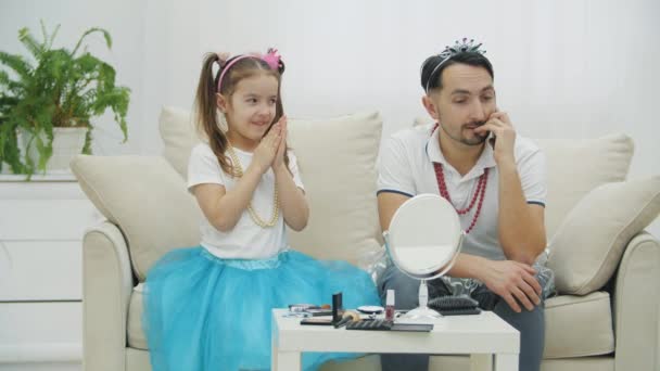 Knappe jongeman is aan de telefoon. Zijn dochter wrijft over haar handen en lacht, klaar om make-up te doen voor haar vader.. — Stockvideo