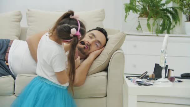 Nettes kleines Kind, das dem Vater rosa Lippenstift auf die Lippen legt, während er schläft. Vater wacht auf, schaut verwirrt und versteht nicht, was passiert ist. — Stockvideo