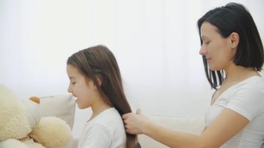 Genç annenin oyuncak ayıyla oynarken kızının saçını taradığı yakın çekim videosu..