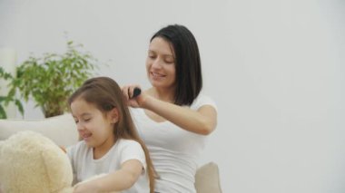 Genç anne oyuncak ayıyla oynarken kızının saçını tarıyor..