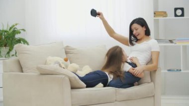 Küçük kız anne ayaklarının üzerinde yatarken anne saçlarını tarıyor, gülümsüyor, çılgınca saç kesimi yapıyor..