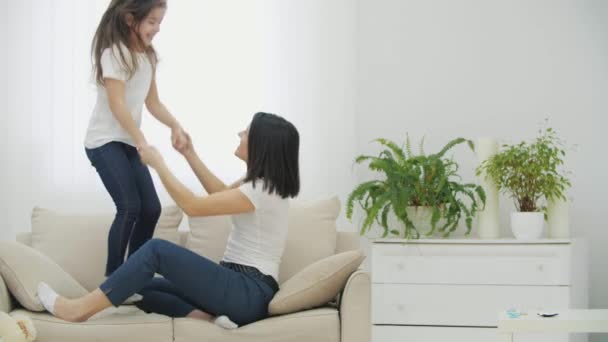 活気のあるお母さんと娘のエネルギー、演奏、ソファの上でジャンプがいっぱいです。. — ストック動画