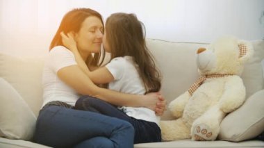 Sevimli küçük kız ve anne birbirlerine sarılıyorlar, gülümsüyorlar, burunlarına dokunuyorlar, sarılıp eğleniyorlar, güneş camdan içeri girerken..