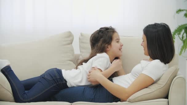 소파에 누워 서로 얼굴을 쓰다듬고 있는 귀여운 딸과 그의 어머니 의대화. — 비디오