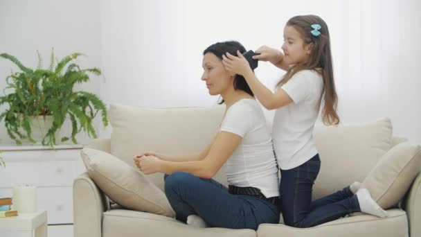 Little cute daughter is combing and braiding her moms hair, doing her a nice hairdo. — Stock Video