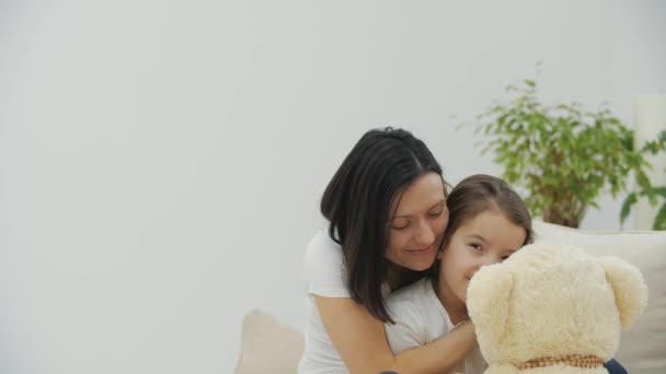 4k видео, где заботливая мать обнимает свою дочь с плюшевым мишкой в руках. — стоковое видео