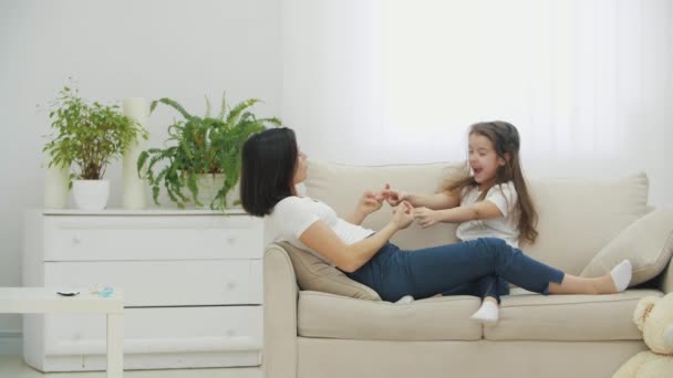 4k video of carefree mother and cute small child daughter tickling and laughing, having fun lying on sofa. — Stock Video