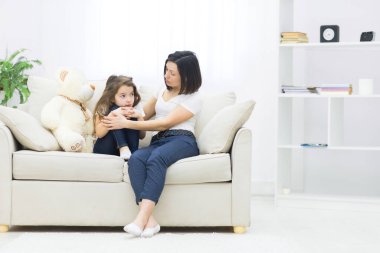 Kanepede oturan üzgün küçük bir kızın fotoğrafı ve annesi ona sarılıyor..