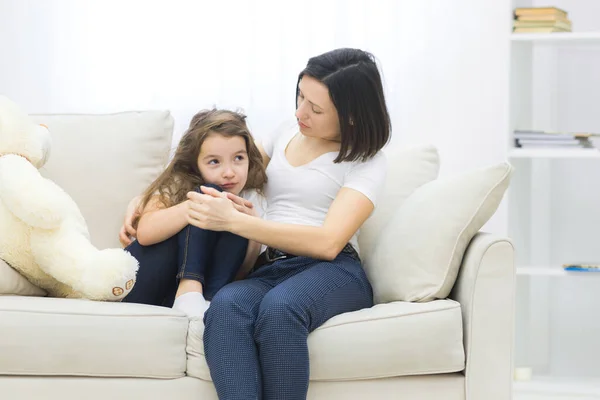 Фото сумної маленької дівчинки, що сидить на дивані і її мама обіймає її . — стокове фото