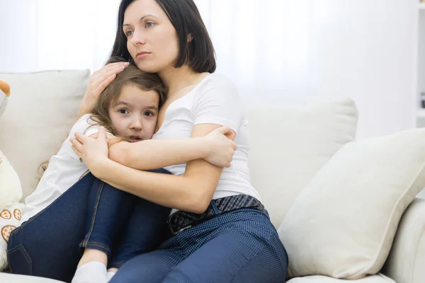 De cerca la foto de la niña triste sentada en el sofá y su mamá abrazándola. — Foto de Stock