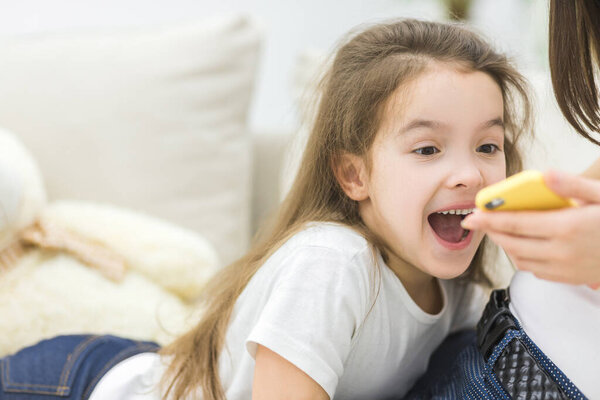 Crop of cute young girl looking on phone with her mom.