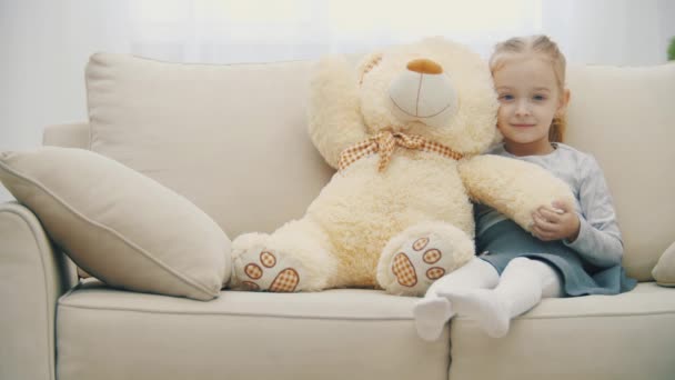 4k slowmotion video van klein meisje op de bank knuffelen haar teddy beer. — Stockvideo