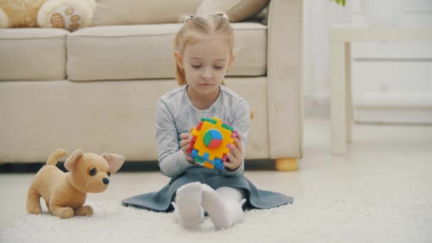 4k cámara lenta de vídeo de la niña sentada en el suelo blanco jugando y luego agitando la mano. — Vídeos de Stock