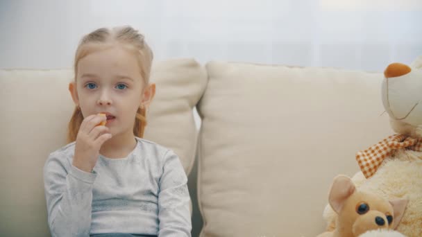 4k slow motion vídeo of little daughter eating sitting on sofa. — Vídeo de Stock