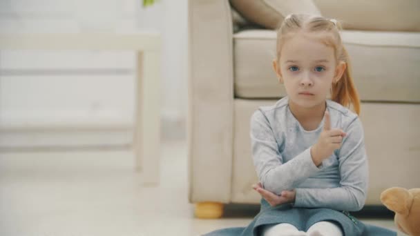 4k video de la niña sentada en el suelo agitando la cabeza y la mano. — Vídeo de stock